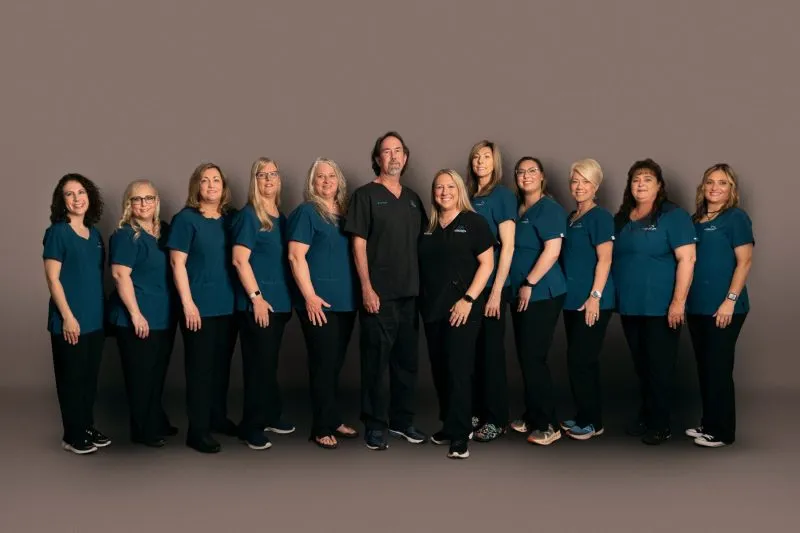 Dental team of thirteen wearing matching teal scrubs, standing together in the office